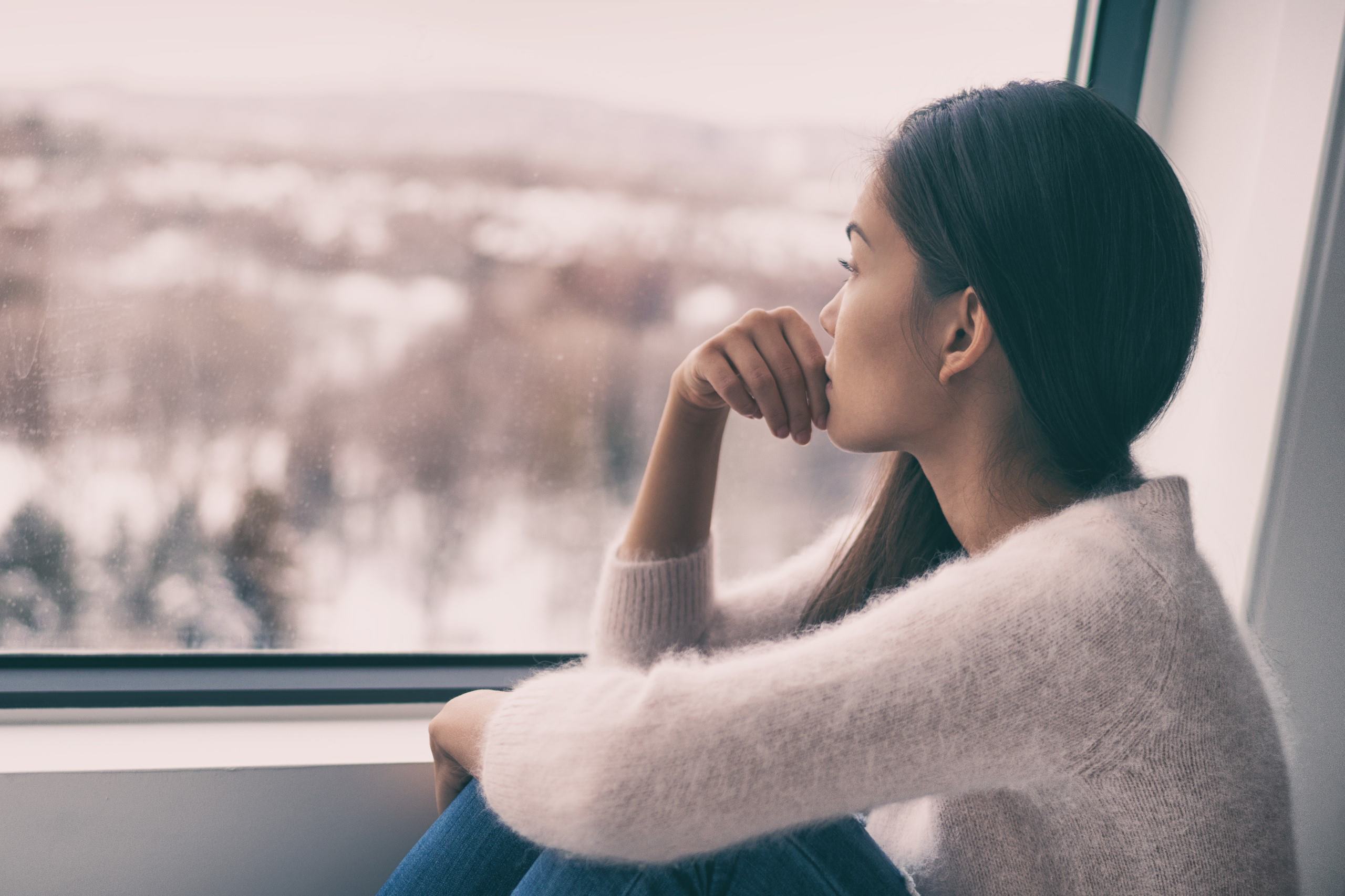 A woman sits looking pensively out of a window.